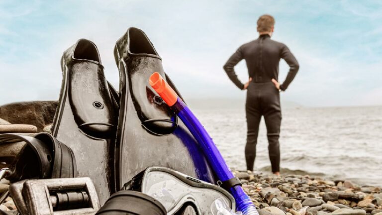 Freediving fins, mask and snorkel on beach near man