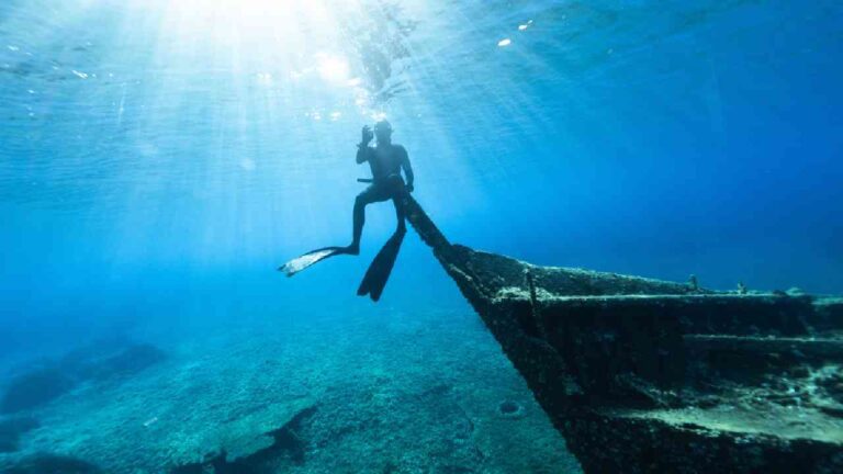 man diving sitting on shipwreck doing the ok symbol